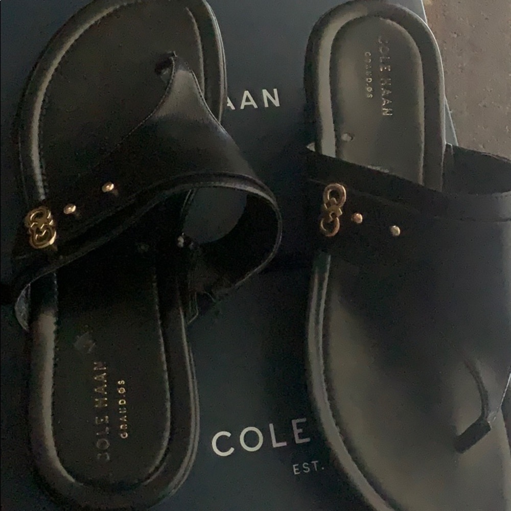 Black Cole Haan flip flops with gold emblem